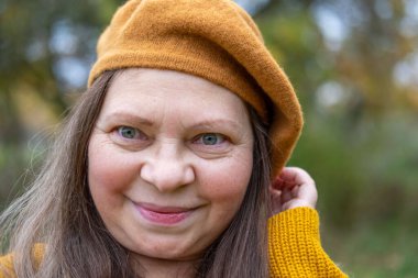 Neşeli, olgun bir kadın eğleniyor, komik bir yüz ifadesi yapıyor, neşeli hareketlerle komik bir resim yapıyor, garip bir ifade sergiliyor, açık havada kendiliğinden çekilen bir an.