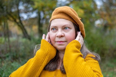 Kulaklarını acılı ifadeyle kaplayan kadın, gürültüden rahatsız olan duygusal portre, çevresel gürültü etkisi portresi, yüksek seslere kendiliğinden tepki, gerçek yüz ifadesi.