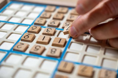 Sayıyı Sudoku yapbozuna dikkatlice yerleştiren eller, meydan okuyucu bulmacaları çözmeye, zihinsel uyarımlara ve klasik oyunlardan keyif almaya kendini kaptırmış yaşlı kişi,