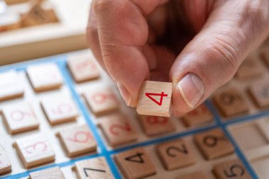 Sayıyı Sudoku yapbozuna dikkatlice yerleştiren eller, meydan okuyucu bulmacaları çözmeye, zihinsel uyarımlara ve klasik oyunlardan keyif almaya kendini kaptırmış yaşlı kişi,