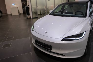 Beyaz Tesla Model 3, fütüristik farlar ve ikonik aerodinamik tasarım modern sergi salonunda sergileniyor, elektrik gücü Elon Musk şirketi Frankfurt 'ta - 25 Ocak 2025