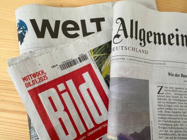 Aralarında Bild, Die Welt ve Allgemeine Zeitung 'un da bulunduğu bir yığın Alman gazetesi, tahtadan bir masanın üzerinde duruyor, basılı medya, Alman medyasını cezbediyor, Frankfurt - 15 Ocak, 2025