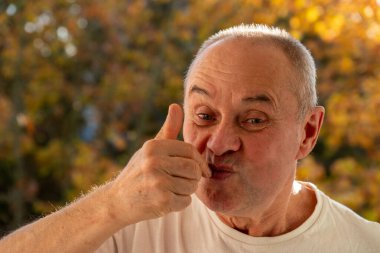 Playful mature man, senior having fun, making funny face, funny freak portrait with playful gestures, whimsical expression, Spontaneous moment captured outdoors clipart