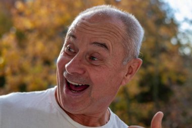 Oyuncu olgun bir adam, son sınıf öğrencisi, eğleniyor, komik surat ifadeleri, neşeli jestleri olan komik bir ucube portresi, garip bir ifade, açık havada kendiliğinden çekilen bir an.