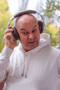 65 yaşında, yaşlı, büyük kulaklıklar takan, müzik dinlerken mutlu bir şekilde gülümseyen, podcast yapan yaşlı bir adam.