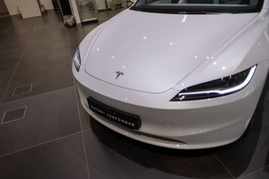 Beyaz Tesla Model 3, fütüristik farlar ve ikonik aerodinamik tasarım modern sergi salonunda sergileniyor, elektrik gücü Elon Musk şirketi Frankfurt 'ta - 25 Ocak 2025