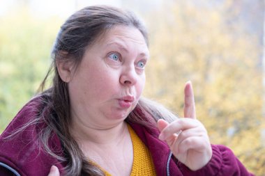 Neşeli, olgun bir kadın eğleniyor, komik bir yüz ifadesi yapıyor, neşeli hareketlerle komik bir resim yapıyor, garip bir ifade sergiliyor, açık havada kendiliğinden çekilen bir an.