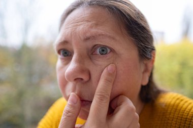 Olgun kadın yüzü kadın 50-55 yaşlarında görünüyor, göz çevresindeki kırışıklıkları inceliyor, göz kenarındaki jestleri, zihinsel yorgunluğu, yaşla ilgili değişiklikleri, hafıza kaybı, estetik bakım, yaşlanma önleyici prosedürleri