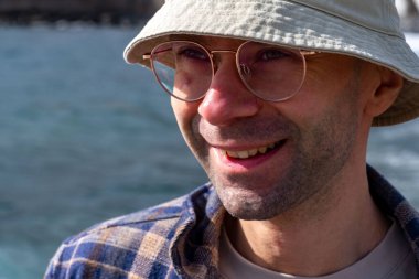 Introspective man stands knee-deep in turquoise waters, Coastal wanderer in checkered shirt and pale bucket hat, experiencing nature's rhythm secluded rocky beach tropical climate zone clipart