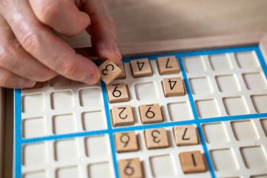 Sayıyı Sudoku yapbozuna dikkatlice yerleştiren eller, meydan okuyucu bulmacaları çözmeye, zihinsel uyarımlara ve klasik oyunlardan keyif almaya kendini kaptırmış yaşlı kişi,