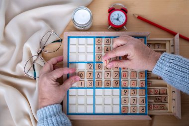 Kadınların ellerini dikkatlice Sudoku bulmacası içine yerleştirirken, meydan okuyan bulmacaları çözmeye kendini kaptırmış yaşlı insanlar, beyin sağlığı, zihinsel aktivite klasik oyunu