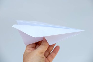 Beyaz kağıt uçak uçuyor, sembol umut ve yeni başlangıçlar, mavi gökyüzüne karşı kadının nazik eli, DIY origami kağıt uçak rüyaları ve özünde uçuşu ve emelleri simgeliyor. 