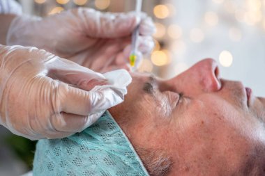 Yaşlanan cilt için kozmetik tedavi, estetik prosedürler, profesyonel yenilenme güzellik uzmanının yaşlı bir adamın yüzüne güzellik iğneleri yapması kırışıklıkları azaltmak ve cildini tazelemek için. 