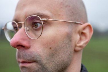 Gözlüklü genç adam başka tarafa bakıyor, yansıtıyor. Göz giyimi tarzı, insan gözleri ve iç gözlem anı, görsel sağlık, çağdaş tarz, entelektüel görünüş, erkek portresi.