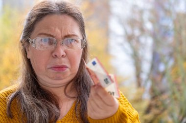 Hayal kırıklığına uğramış 50 yaşında beyaz bir kadın sunuyor, euro banknotlarını sayıyor, elinde az para, nakit ödemeler, tasarruflar, döviz kurları, finansal özgürlükler