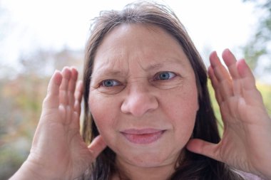 Kulaklarını acılı ifadeyle kaplayan kadın, gürültüden rahatsız olan duygusal portre, çevresel gürültü etkisi portresi, yüksek seslere kendiliğinden tepki, gerçek yüz ifadesi.