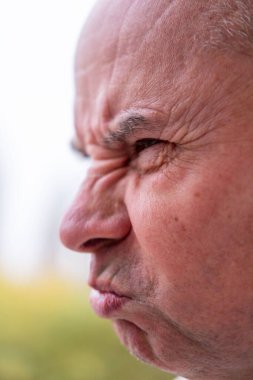 Kızgın yaşlı adam, çatık kaşlı, yoğun bakışlı ve büzüşmüş dudaklı. Ciddi kıdemli adam agresif ve üzgün görünüyor, güçlü duygularını ifade ediyor, saldırganlığı, gerilimi ve yüzleşmeyi kavrıyor.