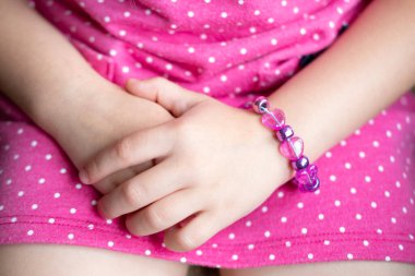 Boncuklu bilezik takan çocuk elleri. Pembe benekli elbise. Elleri yakın çekim. Masumiyet ve çocukluk, neşeli cazibeli pembe elbise ve bilezik