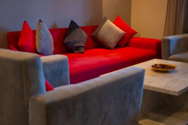 Rahat oturma odasında renkli yastıkları olan kırmızı kanepe, rahat ve şık iç mekanı sembolize ediyor, otel odası, daire, tatil kirası, otelde parlak oda, konforlu konaklama