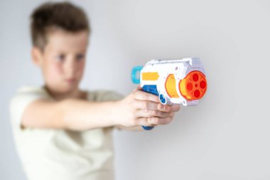 yakın plan oyuncak silah, arka planda tutan genç bir çocuk, oyuna çocuk perspektifi, askeri oyuncaklar sahne donanımı, saldırganlık ve genç zihinler, ebeveynlik ve davranış gelişimi üzerindeki etkisi