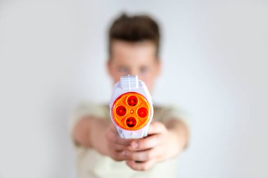yakın plan oyuncak silah, arka planda tutan genç bir çocuk, oyuna çocuk perspektifi, askeri oyuncaklar sahne donanımı, saldırganlık ve genç zihinler, ebeveynlik ve davranış gelişimi üzerindeki etkisi