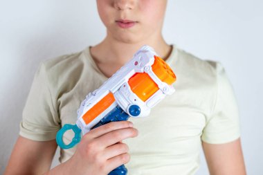 yakın plan oyuncak silah, arka planda tutan genç bir çocuk, oyuna çocuk perspektifi, askeri oyuncaklar sahne donanımı, saldırganlık ve genç zihinler, ebeveynlik ve davranış gelişimi üzerindeki etkisi
