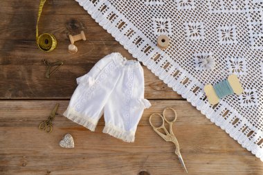 Viktorya dönemi oyuncak bebek iç çamaşırları, el yapımı tarihi bebek iç çamaşırı seti dantelli klasik bebek iç çamaşırı kırsal ahşap arka planda el yapımı dikiş aksesuarları. Retro-stil işçilik kavramı