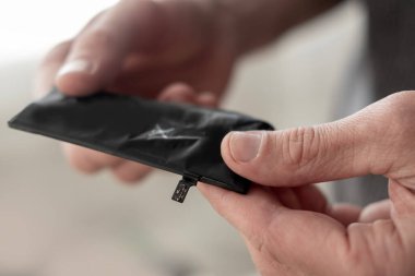 Ellerinde şişmiş telefon bataryası var, hasar var. Batarya arızası, onarım ve değiştirme, şişmiş akıllı telefon pili, şişkinlik sorunu