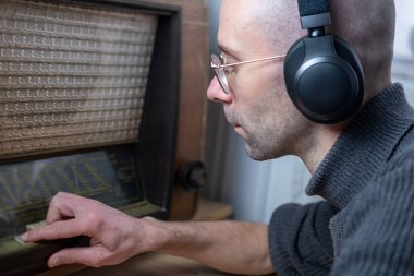 Kablosuz kulaklıklı olumlu genç adam, 60 'ların eski klasik radyosunu dinlerken mutlu bir şekilde müzik, podcast, Retro estetik