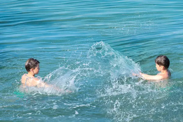 İki küçük çocuk, kardeşler denizde sıçrayıp oynuyorlar, güneşli yaz gününde okyanus dalgaları, aile aktiviteleri, su maceraları çocuklarda merak ve çevreye olan sevgiyi arttırıyorlar.