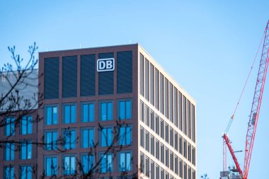 Mavi gökyüzüne karşı belirgin DB logosu olan modern bina, Deutsche Bahn şirketinin ulaşım ve bağlantıları, inşaat vinçleri olan şehir manzarası, Frankfurt - 19 Ocak 2025