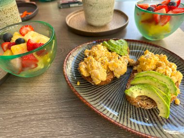 Avokado tostlu kahvaltı, çırpılmış yumurta, meyve salatası, sağlıklı yemek, kafe ziyafeti, brunch zamanı, besleyici ve lezzetli yemekler için taze malzemeler, sağlıklı ve renkli tabaklar.
