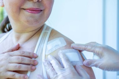 Doktor, cerrahi yarayı, kadın hastayı, omuz yaralanmasını, steril aletleri, iyileşme sürecini, klinik hijyeni, ameliyat sonrası bakımı, tıbbi profesyonel temizlik prosedürünü, 