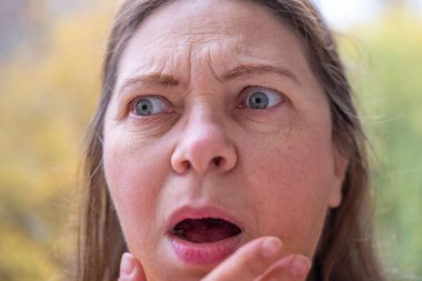 Yakın plan orta yaşlı kadın şok olmuş ve şaşkın bir ifadeyle, geniş gözler ve açık bir ağızla derin bir şaşkınlık, duygusal dramatik bir portre, şaşkınlık ve huşu sergiliyor.