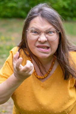 Saldırgan orta yaşlı kadın dışarıda negatif duygular sergiliyor. Çevresi yeşillik ve dingin çevreyle çevrili. Öfke ve gerilimle reaksiyon gösteriyor.