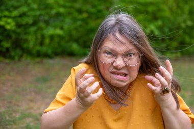 Saldırgan orta yaşlı kadın dışarıda negatif duygular sergiliyor. Çevresi yeşillik ve dingin çevreyle çevrili. Öfke ve gerilimle reaksiyon gösteriyor.