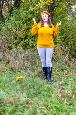 Pozitif orta yaşlı kadın, hardal kıyafetli, temiz havanın tadını çıkarıyor, sonbaharda orman, sonbahar havası, mutluluk doğa yürüyüşü, sonbaharın tadını çıkarıyor, gülümsüyor, neşeli bir ifade, açık havada, açık havada olgun bir portre