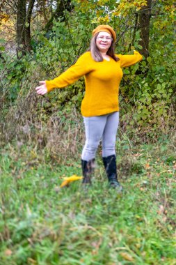 Pozitif orta yaşlı kadın, hardal kıyafetli, temiz havanın tadını çıkarıyor, sonbaharda orman, sonbahar havası, mutluluk doğa yürüyüşü, sonbaharın tadını çıkarıyor, gülümsüyor, neşeli bir ifade, açık havada, açık havada olgun bir portre