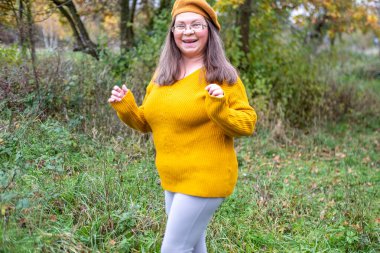 Pozitif orta yaşlı kadın, hardal kıyafetli, temiz havanın tadını çıkarıyor, sonbaharda orman, sonbahar havası, mutluluk doğa yürüyüşü, sonbaharın tadını çıkarıyor, gülümsüyor, neşeli bir ifade, açık havada, açık havada olgun bir portre