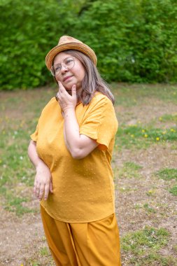 Şık, yaşlı, mutlu, sarı kıyafetli, şapkalı, hardallı, açık havada gülümseyen olgun bir kadın. Yaz ya da bahar, doğal görünüş, günlük yaşam tarzı, gerçek kadınlar için moda.