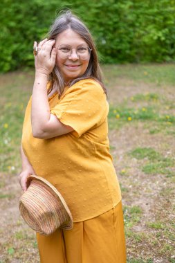 Şık, yaşlı, mutlu, sarı kıyafetli, şapkalı, hardallı, açık havada gülümseyen olgun bir kadın. Yaz ya da bahar, doğal görünüş, günlük yaşam tarzı, gerçek kadınlar için moda.