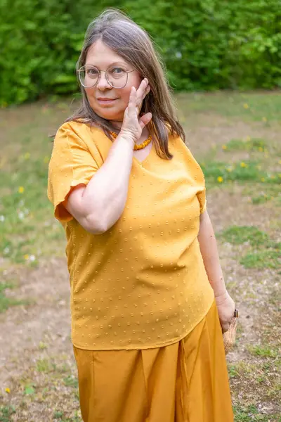 Şık, yaşlı, mutlu, sarı kıyafetli, şapkalı, hardallı, açık havada gülümseyen olgun bir kadın. Yaz ya da bahar, doğal görünüş, günlük yaşam tarzı, gerçek kadınlar için moda.