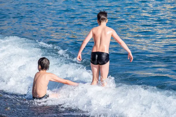 İki küçük çocuk, iki genç erkek çocuk denize dalıp oynuyorlar güneşli bir yaz gününde okyanus dalgaları, aile aktiviteleri, su maceraları çocuklarda merak ve çevreye olan sevgiyi arttırıyor. 