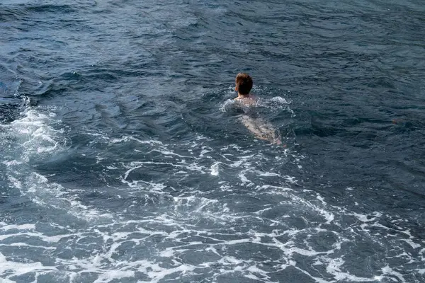 Çocuk denizde neşeyle yüzüyor, yaz tatilinin tadını çıkarırken su güvenliği becerilerini öğreniyor, çocuk deniz dalgalarında oynuyor, kaygısız ve mutlu, ebeveynler güvenliği ve boğulma riskini göze alıyor.