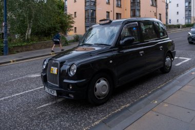 Siyah klasik İngiliz taksisi Edinburgh caddesinde, geleneksel taksi, tarihi mimari, miras atmosferi, ulaşım ikonu, seyahat havası, sokak fotoğrafçılığı, Edinburgh, İngiltere - 15 Nisan 2025