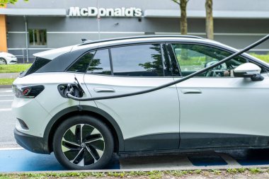 Beyaz Volkswagen ID. 4 SUV Almanya 'da şehir caddesinde şarj ediliyor, Avrupa' da elektrikli araba, çevre dostu ulaşım, temiz enerji aracı, son teknoloji otomotiv, Frankfurt - 21 Nisan 2025