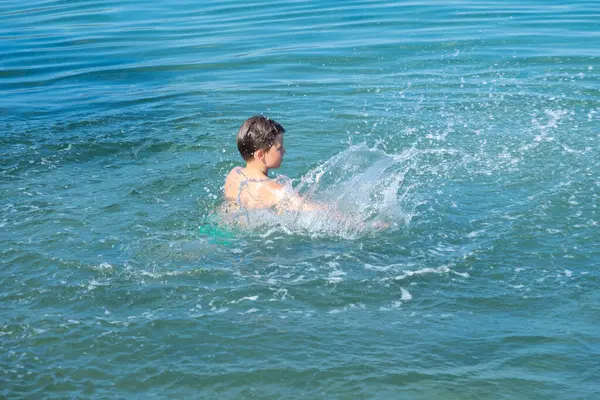 Çocuk denizde neşeyle yüzüyor, yaz tatilinin tadını çıkarırken su güvenliği becerilerini öğreniyor, çocuk deniz dalgalarında oynuyor, kaygısız ve mutlu, ebeveynler güvenliği ve boğulma riskini göze alıyor. 