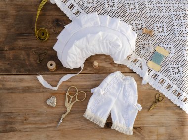 Viktorya dönemi oyuncak bebek iç çamaşırları, el yapımı tarihi bebek iç çamaşırı seti dantelli klasik bebek iç çamaşırı kırsal ahşap arka planda el yapımı dikiş aksesuarları. Retro-stil işçilik kavramı