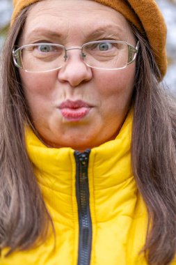 Yakın plan portresi son sınıf öğrencisi bir kadının aptal suratını çıkarması komik bir dil çıkarması komik surat buruşturması yaşlanan mizah kırışıklıkları sonbahar havası, komik yüzlü ve neşeli ruhlu yaşlı bir kadının doğal yakınlığı. 