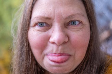 Yakın plan portresi son sınıf öğrencisi bir kadının aptal suratını çıkarması komik bir dil çıkarması komik surat buruşturması yaşlanan mizah kırışıklıkları sonbahar havası, komik yüzlü ve neşeli ruhlu yaşlı bir kadının doğal yakınlığı. 